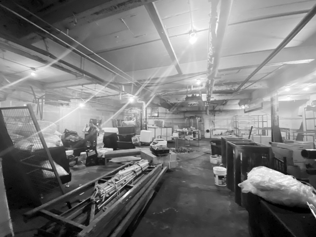 Black and white photograph of an industrial floor interior, cluttered and waiting